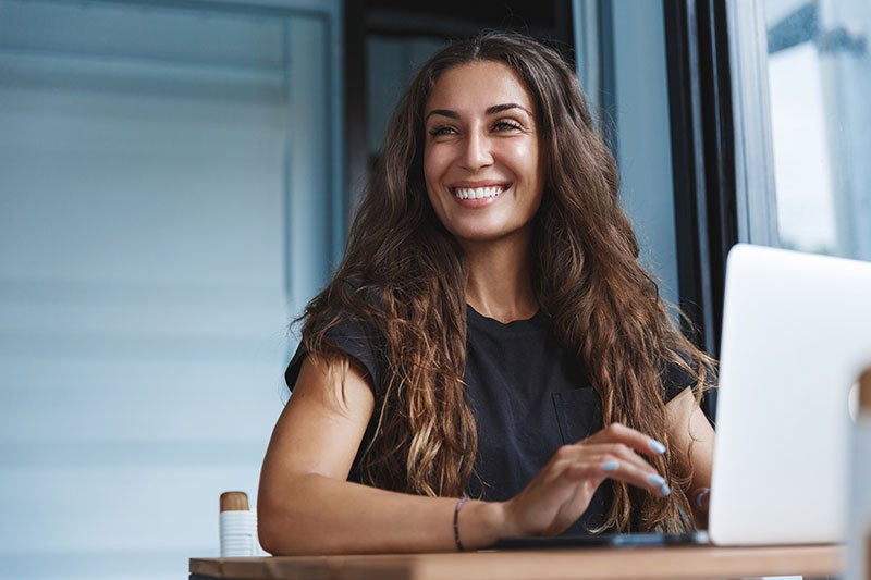 Mujer sonriente, feliz, sentada frente a una computadora portátil